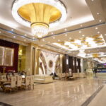 Lavish banquet hall interior with grand golden chandeliers, luxurious seating arrangements, marble flooring, and opulent ceiling design.